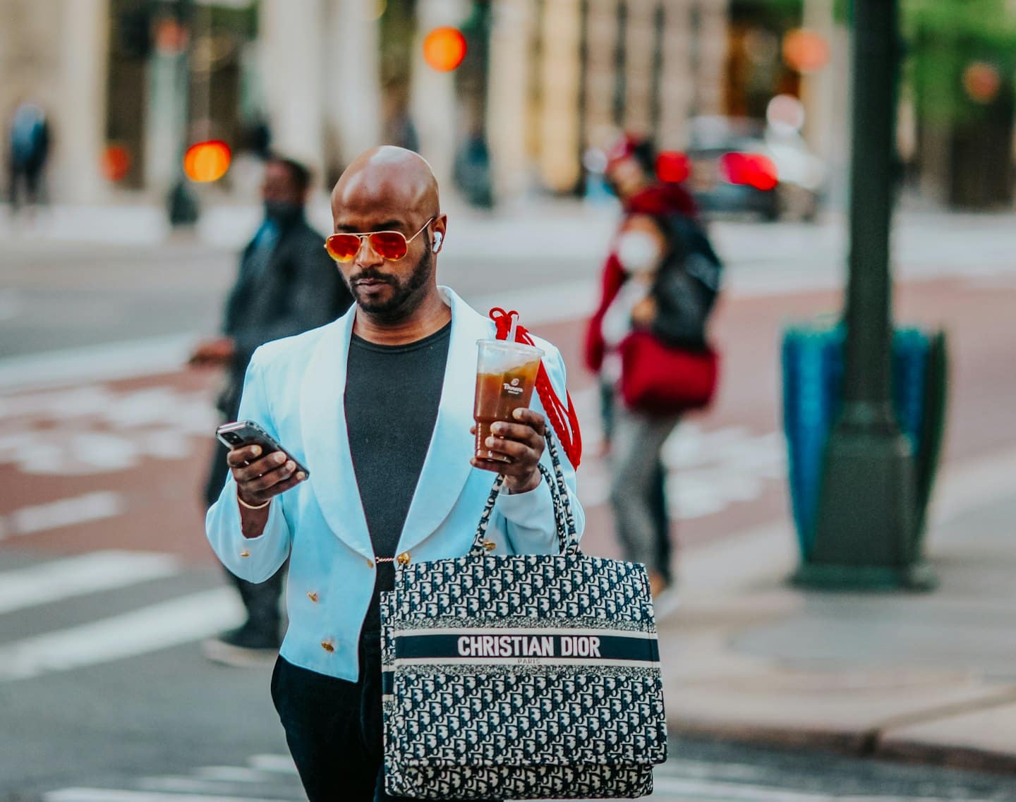 Man in blue blazer walks in city checking smartphone.