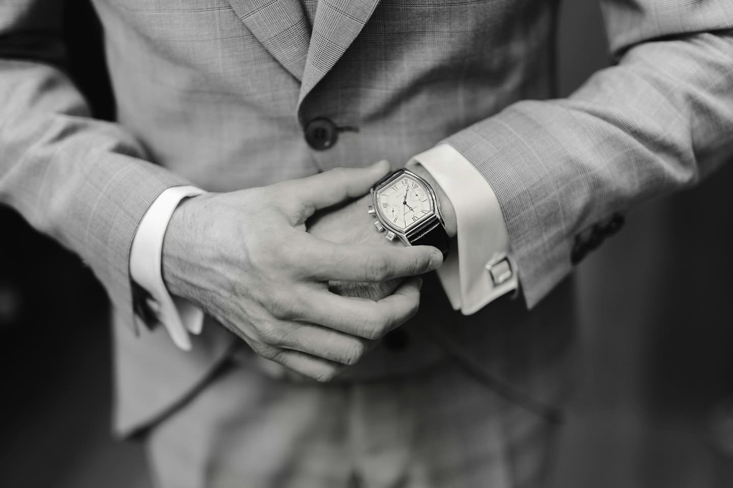A man in a suit adjusts a leather watch.