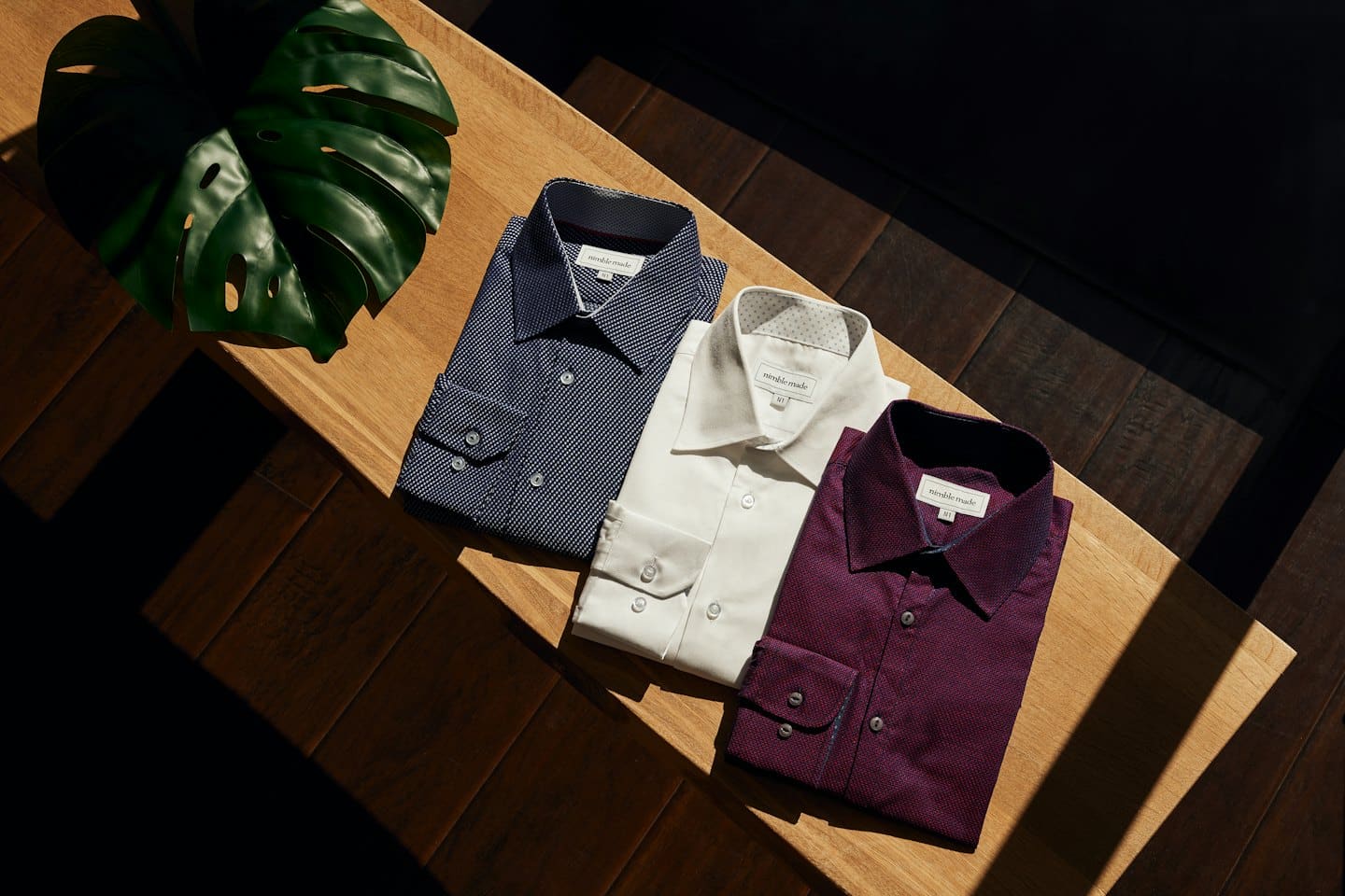 Three folded men's dress shirts on a wooden surface.
