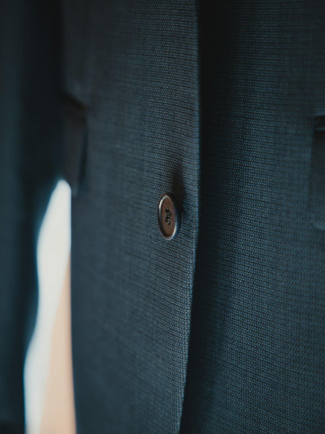 Brown button on the navy blue fabric of a suit jacket.